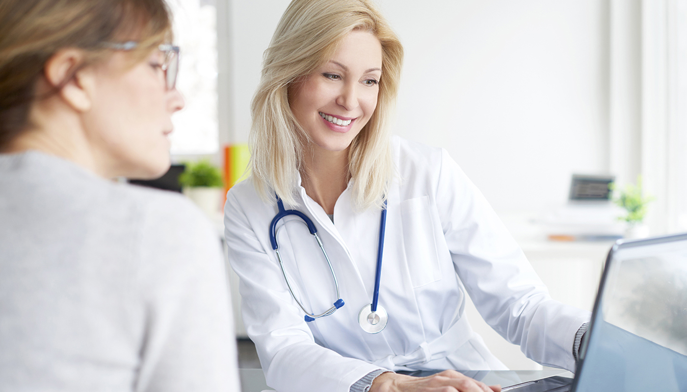 A woman in white lab coat and stethoscope sitting next to another person.