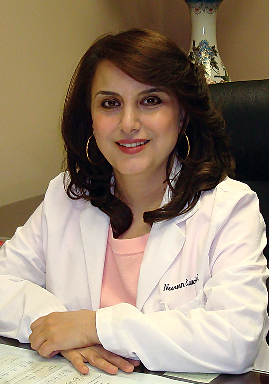 A woman in white lab coat sitting at desk.