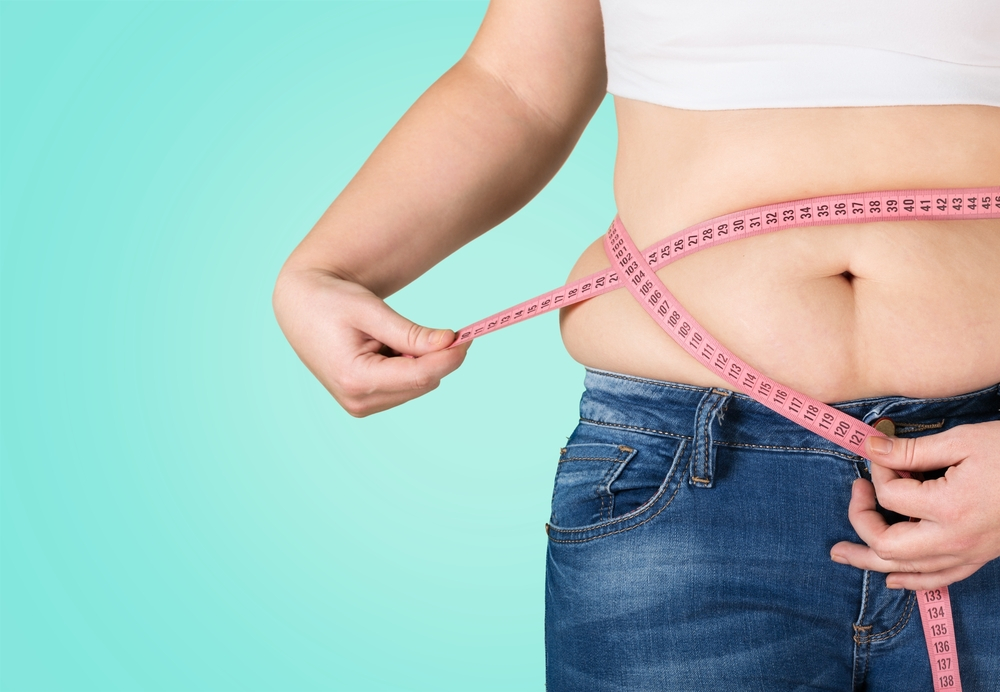 A woman is measuring her waist with a pink tape.